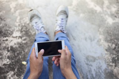 Gerilmiş bacaklarla oturan ve akıllı telefon kullanan bir erkek gencin sadece el ve bacaklarını kapatın.