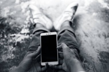 Gerilmiş bacaklarla oturan ve akıllı telefon kullanan bir erkek gencin sadece el ve bacaklarını kapatın.