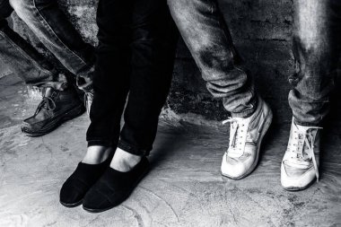 Duvarda oturan ve arkadaşlarıyla vakit geçiren akıllı telefonları kullanan çok ırklı gençlerin sadece bacaklarını kapatın.