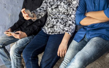 Bir duvarda oturan ve akıllı telefonlar kullanarak ve arkadaşlarınızla vakit geçirmek genç sadece elleri ve bacakları kapatın.