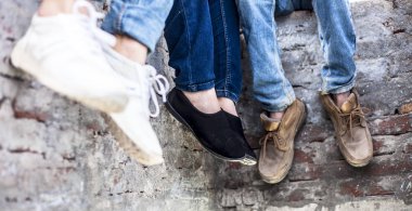 Duvarda oturan ve arkadaşlarıyla vakit geçiren akıllı telefonları kullanan çok ırklı gençlerin sadece bacaklarını kapatın.