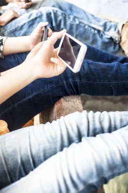 Bir duvarda oturan ve akıllı telefonlar kullanarak ve arkadaşlarınızla vakit geçirmek genç sadece elleri ve bacakları kapatın.