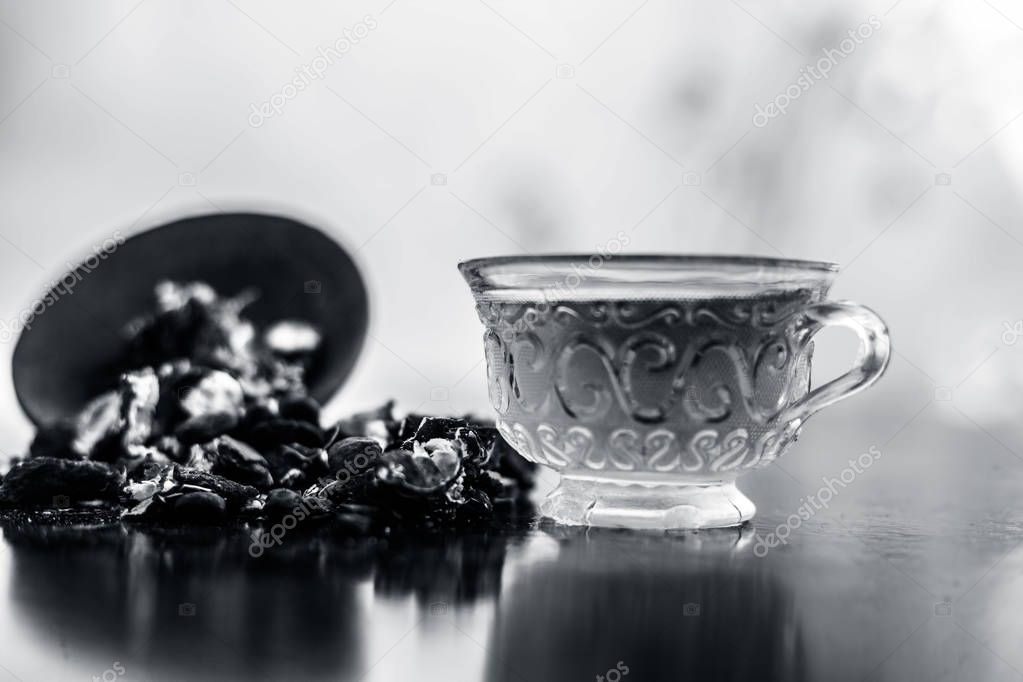 Tamarind or imli or amli in a clay bowl along with its roasted seeds and extract tea in a transparent glass cup with mint or mentha leaves on top on wooden surface.