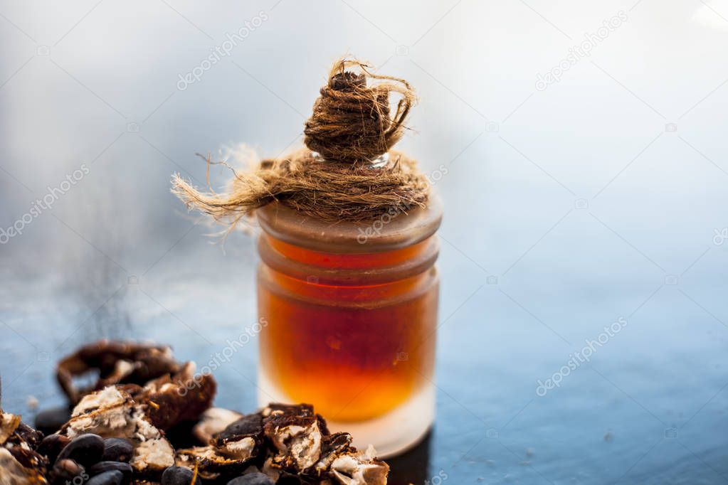 Tamarind or imli or amli in a clay bowl along with its roasted seeds and extract essential oil in a glass bottle on wooden surface.