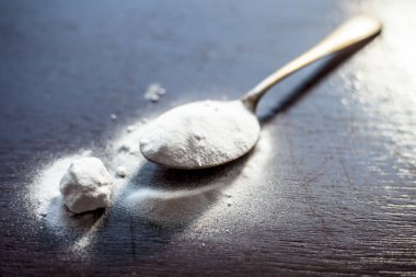 Kahverengi renkli ahşap yüzey üzerinde altın renkli pirinç kaşık ham kabartma tozu veya Sodyum bikarbonat.