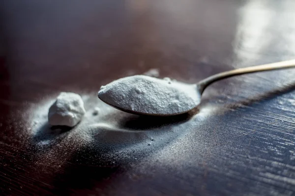 Raw baking soda or baking powder in a golden colored spoon on wooden surface.