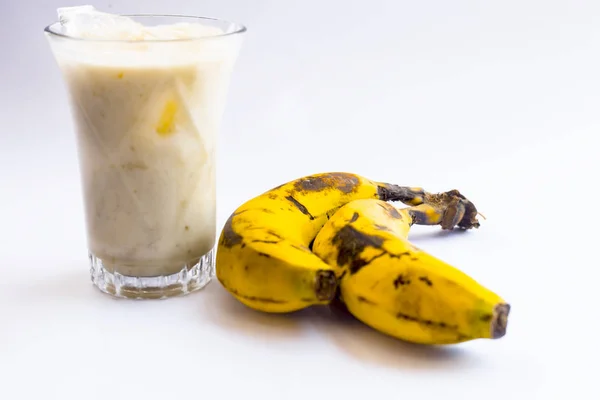 生の有機新鮮なバナナとそのスムージーまたはシェイクまたはバナナミルクを白に分離したグラスで — ストック写真