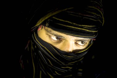 Striking portrait of male teenager isolated on black with piercing expressive eyes along with a cloth covering face except eyes.Expressing boldness and blondness. clipart