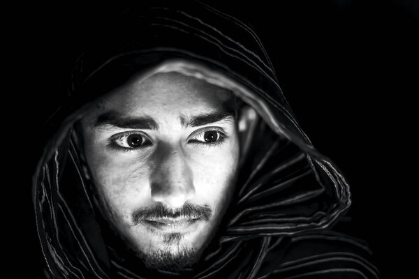 Portrait shot of man in black and white color isolated on black expressing angriness on his face and wearing black colored cloth on his face.