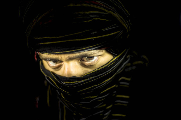 Striking portrait of male teenager isolated on black with piercing expressive eyes along with a cloth covering face except eyes.Expressing boldness and blondness.