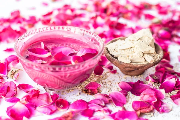 Rose flower face pack isolated with rose petals well mixed with mulpani mitti or fuller\'s earth in a glass bowl and entire ingredients present on the surface,Used to  soak excess oil from face.