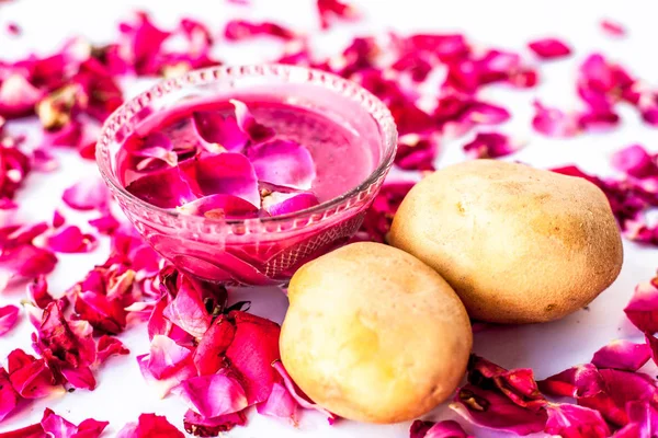 Best face mask or face pack to reduce blemishes and dark patches isolated on white i.e. Rose petals well mixed with potato juice in a bowl and raw potato and rose petals present on the surface.