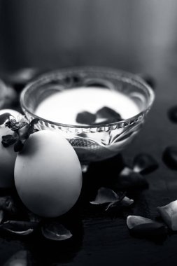 Anti-aging yüz paketi yani süt ve yumurta yüz paketi parlak siyah yüzeyüzerinde bir cam kase bazı gül yaprakları ve tüm bileşenleri ile.