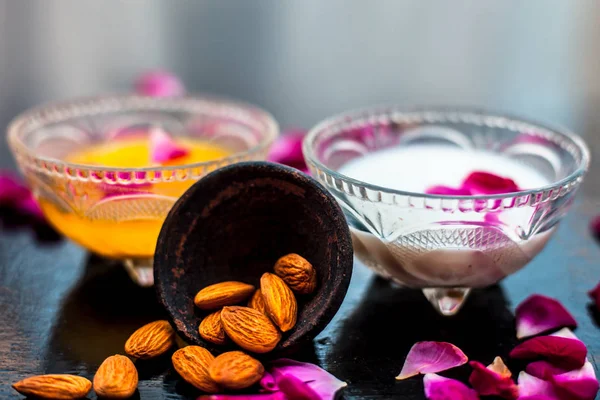 Rose and milk face pack on black colored shiny surface consisting of rose water,almonds and honey in a glass bowl and entire raw ingredients on the surface.Used for instant glow.