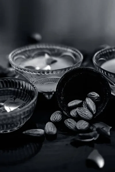 Rose and milk face pack on black colored shiny surface consisting of rose water,almonds and honey in a glass bowl and entire raw ingredients on the surface.Used for instant glow.