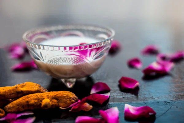 Milk face pack on black shiny surface consisting of raw milk,turmeric or haldi and badam in a glass bowl along with entire raw ingredients.