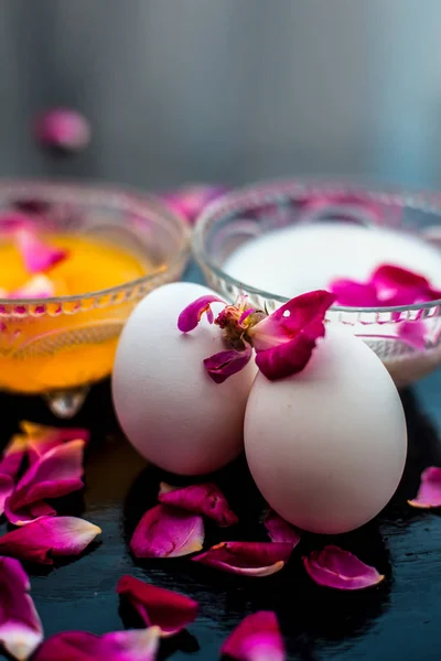 Anti-aging face pack i.e.  Milk and egg face pack in a glass bowl on shiny black surface with some rose petals and entire of its constituents with it.