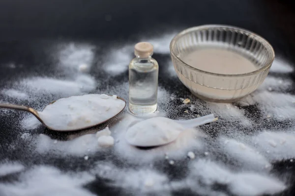 Face mask or face pack of baking soda in a glass bowl on wooden surface along with powder and some coconut oil in a transparent glass bottle. Used for rashes. Horizontal shot.