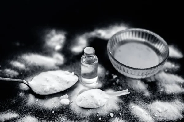 Face mask or face pack of baking soda in a glass bowl on wooden surface along with powder and some coconut oil in a transparent glass bottle. Used for rashes. Horizontal shot.