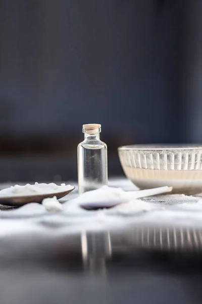 Face mask or face pack of baking soda in a glass bowl on wooden surface along with powder and some coconut oil in a transparent glass bottle. Used for rashes. Vertical shot with shallow depth of field