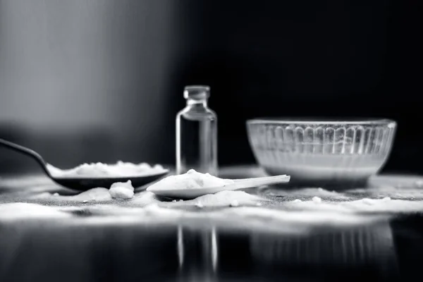 Face mask or face pack of baking soda in a glass bowl on wooden surface along with powder and some coconut oil in a transparent glass bottle. Used for rashes,horizontal shot with depth of field.