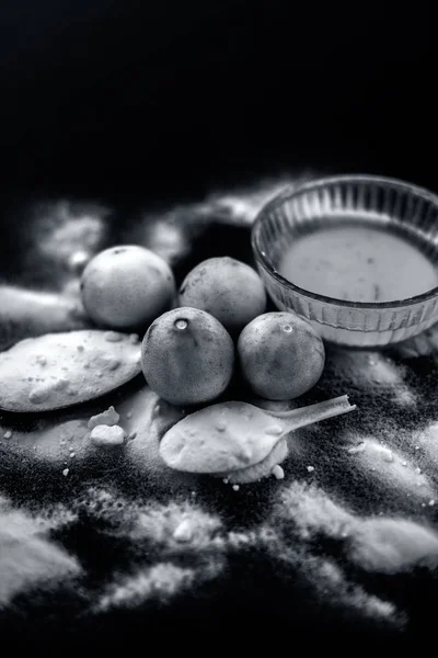 Baking soda face mask in a glass bowl on wooden surface along with some baking soda sprinkled on the surface and lemons also on surface. Used to blemishes skin instantly.