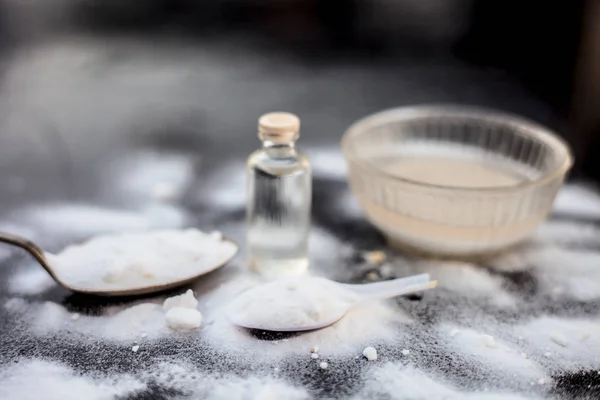 Face mask or face pack of baking soda in a glass bowl on wooden surface along with powder and some coconut oil in a transparent glass bottle. Used for rashes. Horizontal shot.