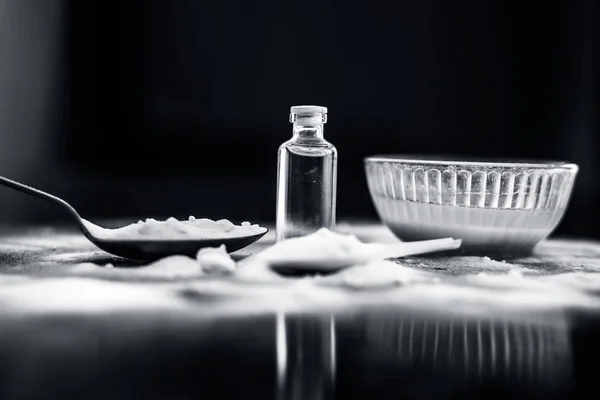 Face mask or face pack of baking soda in a glass bowl on wooden surface along with powder and some coconut oil in a transparent glass bottle. Used for rashes. Horizontal shot.