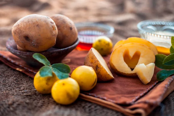 Glowing face mask of potato juice in a glass bowl on brown colored surface along with some lemon juice,potato juice and honey.Horizontal shot.