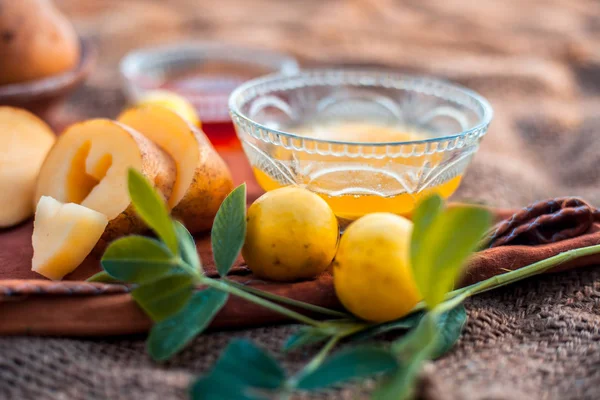 Glowing face mask of potato juice in a glass bowl on brown colored surface along with some lemon juice,potato juice and honey.Horizontal shot.