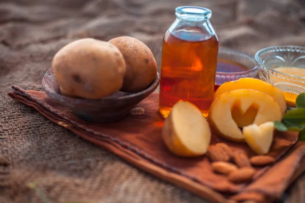 Glowing face mask of potato juice in a glass bowl on brown colored surface along with some Potato juice,honey and almond oil.Horizontal shot.To eliminate skin rashes, remove impurities,etc.