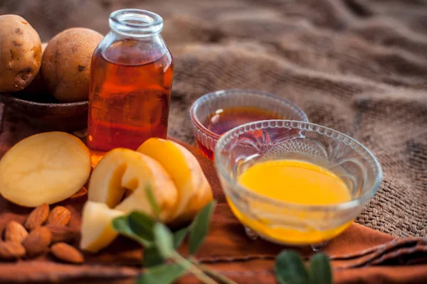 Glowing face mask of potato juice in a glass bowl on brown colored surface along with some Potato juice,honey and almond oil.Horizontal shot.To eliminate skin rashes, remove impurities,etc.