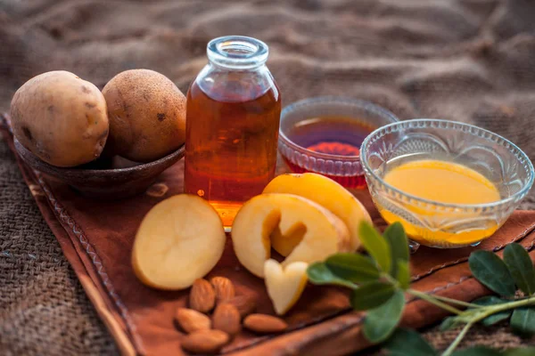 Glowing face mask of potato juice in a glass bowl on brown colored surface along with some Potato juice,honey and almond oil.Horizontal shot.To eliminate skin rashes, remove impurities,etc.