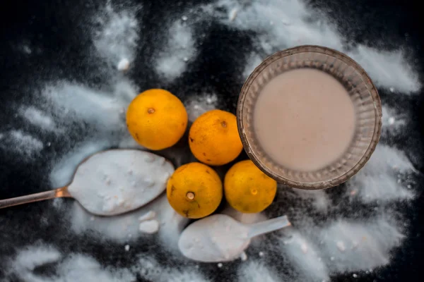 Baking soda face mask in a glass bowl on wooden surface along with some baking soda sprinkled on the surface and lemons also on surface. Used to blemishes skin instantly.Horizontal top shot.