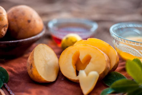 Glowing face mask of potato juice in a glass bowl on brown colored surface along with some lemon juice,potato juice and honey.Horizontal shot.