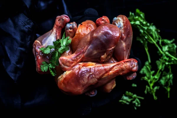 Raw cut unwashed chicken drumsticks in a steel plate isolated in black along with bunch of fresh parsley or coriander leaves on it. Vertical close up shot.