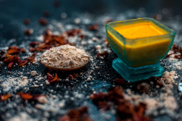 Face mask for skin whitening on wooden surface consisting of besan or gram flour and some rose water. With some dried rose petals and gram flour spread on the surface.