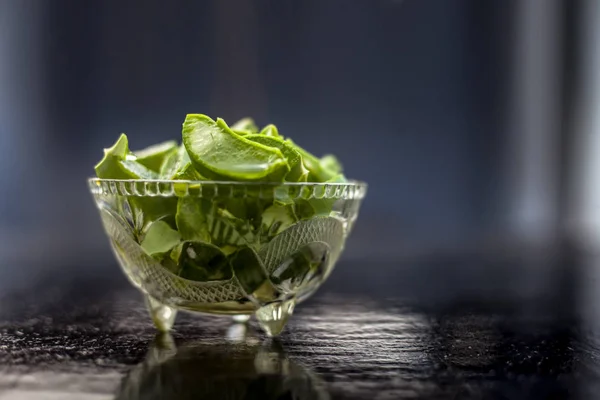 Raw cut aloevera or aloe vera gel in a glass bowl on wooden surface along with its reflection on the surface.