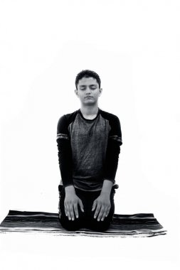 Siyah renkli kıyafetleri giyen ve renkli geleneksel mat yoga yapıyor ve ünlü Vajrasana veya Diamond Pose beyaz üzerinde izole genç çocuk. Dikey izole çekim.