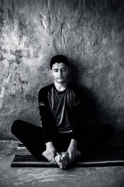 Genç çocuk siyah renkli kıyafetleri giyiyor ve renkli geleneksel mat yoga yapıyor ve ateş log Pose yapıyor (Agni Stambhasana) göz kapalı ve kaba duvara karşı. Yatay çekim.