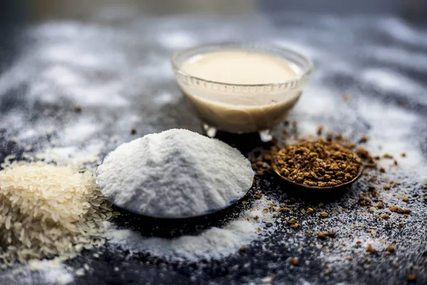 Hair growth remedy of rice flour water and fenugreek/coriander/parsley seeds powder on wooden surface and its paste in a glass bowl with some rice flour spread on the surface. Horizontal shot.