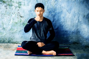 Siyah kıyafetleri giyen renkli bir mat Pranayama veya Pranayam veya nefes kontrol yoga yapan genç adamın portre çekimi.
