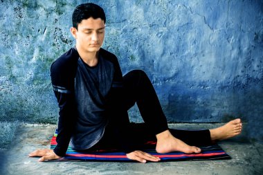 Balıkların Yarı Efendisi Pose veya Ardha Matsyendrasana siyah kıyafetleri giyerek renkli paspas üzerinde beyaz bir genç adam tarafından gerçekleştirilen.