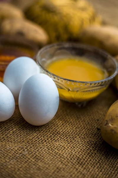 potato juice well mixed with honey and egg yolks in bowls along raw potatoes and eggs on wooden surface,  concept  of homemade all-rounder hair growth remedy which will act as a conditioner as well as hair growth promoter