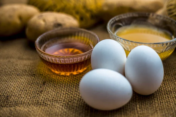 potato juice well mixed with honey and egg yolks in bowls along raw potatoes and eggs on wooden surface,  concept  of homemade all-rounder hair growth remedy which will act as a conditioner as well as hair growth promoter