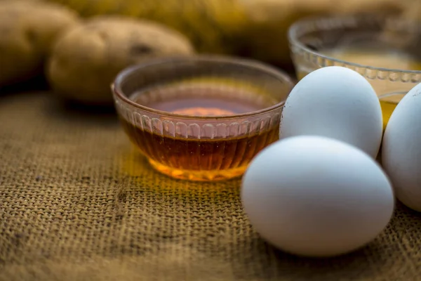 土豆汁与蜂蜜和蛋黄混合在碗中沿生土豆和鸡蛋在木表面 概念自制的全能头发生长补救措施 这将作为一个调理剂以及头发生长促进剂 — 图库照片