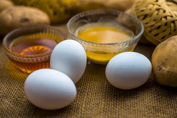 土豆汁与蜂蜜和蛋黄混合在碗中沿生土豆和鸡蛋在木表面 概念自制的全能头发生长补救措施 这将作为一个调理剂以及头发生长促进剂 — 图库照片