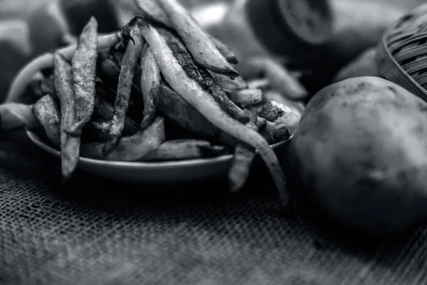 fried cut french fries in glass plate with raw potatoes on burlap surface