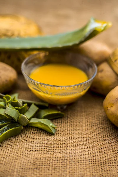 potatoes juice well mixed with aloe vera gel in glass bowl along raw potatoes and aloe vera leaves on jute bag surface, concept  of homemade conditioner and shampoo for dandruff and scalp cleaning