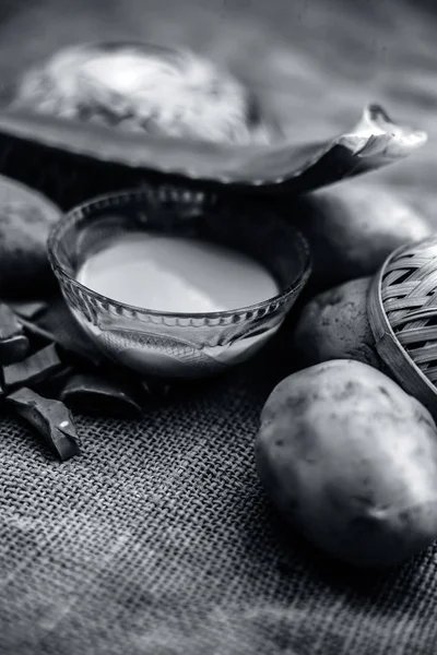 potatoes juice well mixed with aloe vera gel in glass bowl along raw potatoes and aloe vera leaves on jute bag surface, concept  of homemade conditioner and shampoo for dandruff and scalp cleaning